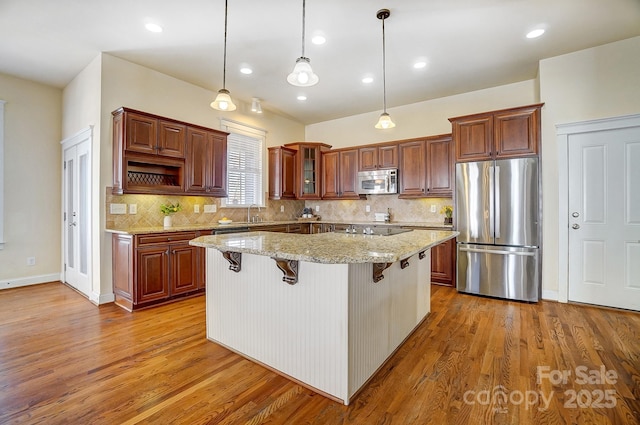 kitchen with glass insert cabinets, a center island, light stone countertops, stainless steel appliances, and a kitchen bar