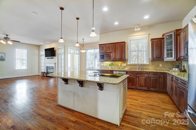 kitchen with a breakfast bar area, a sink, a kitchen island, light stone countertops, and glass insert cabinets