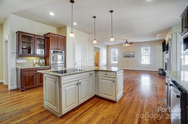 kitchen featuring glass insert cabinets, open floor plan, a center island with sink, and black electric stovetop