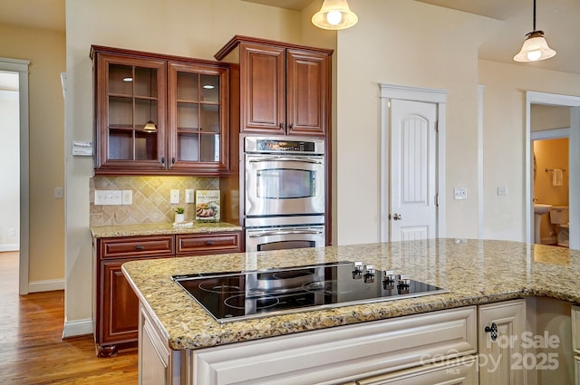 kitchen with tasteful backsplash, glass insert cabinets, hanging light fixtures, black electric cooktop, and double oven