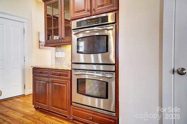 kitchen featuring double oven, brown cabinetry, and glass insert cabinets