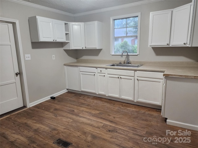 kitchen featuring dark wood-type flooring, a textured ceiling, ornamental molding, white cabinets, and sink