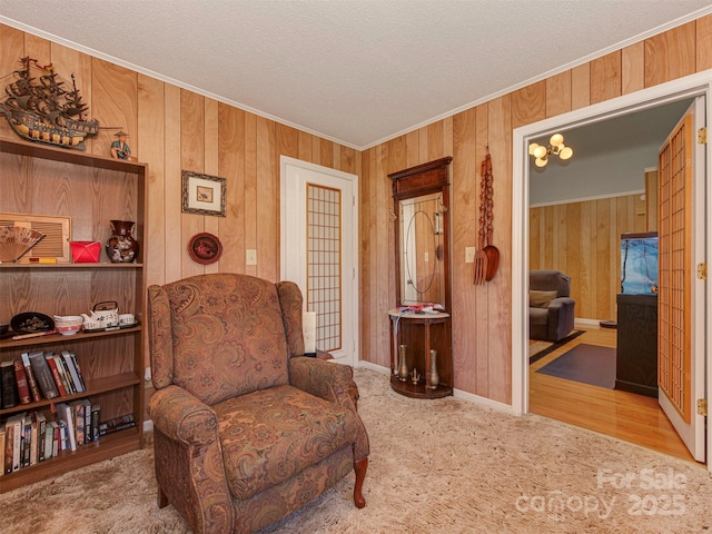 sitting room with wood walls, a textured ceiling, crown molding, and carpet flooring