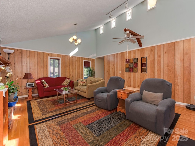 living room with ceiling fan with notable chandelier, rail lighting, a textured ceiling, and high vaulted ceiling