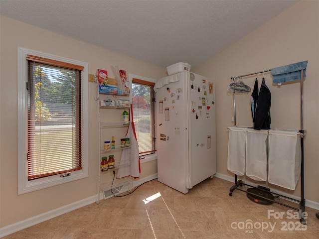 interior space with a textured ceiling, white fridge, and vaulted ceiling