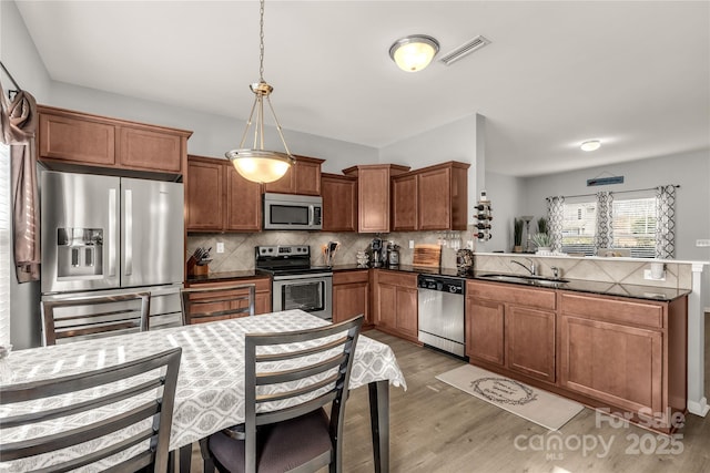 kitchen featuring appliances with stainless steel finishes, decorative light fixtures, tasteful backsplash, light hardwood / wood-style floors, and sink