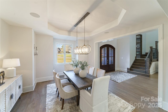 dining space featuring french doors, a raised ceiling, an inviting chandelier, and dark hardwood / wood-style floors