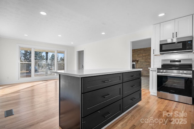 kitchen with white cabinets, a center island, stainless steel appliances, backsplash, and light hardwood / wood-style flooring