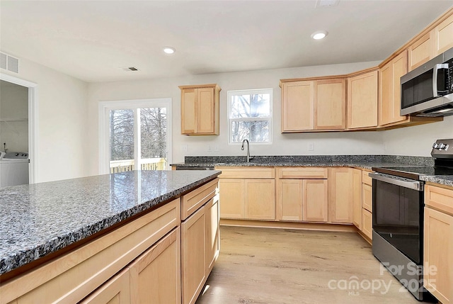 kitchen with stainless steel appliances, light brown cabinets, light wood-type flooring, dark stone countertops, and sink