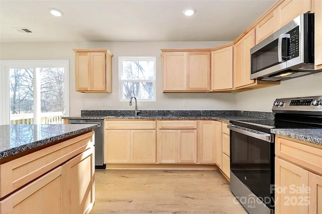 kitchen with stainless steel appliances, light wood-type flooring, light brown cabinetry, dark stone counters, and sink