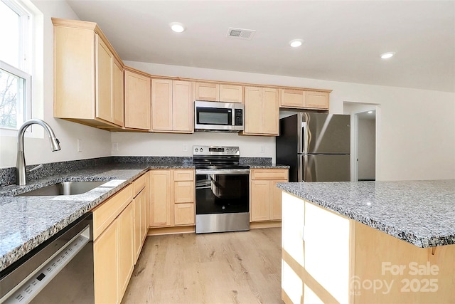 kitchen featuring light brown cabinets, stainless steel appliances, light hardwood / wood-style floors, sink, and light stone counters