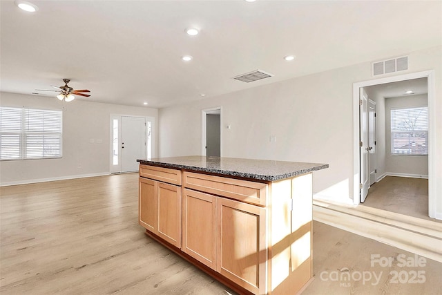 kitchen featuring ceiling fan, light brown cabinets, light wood-type flooring, dark stone counters, and a kitchen island