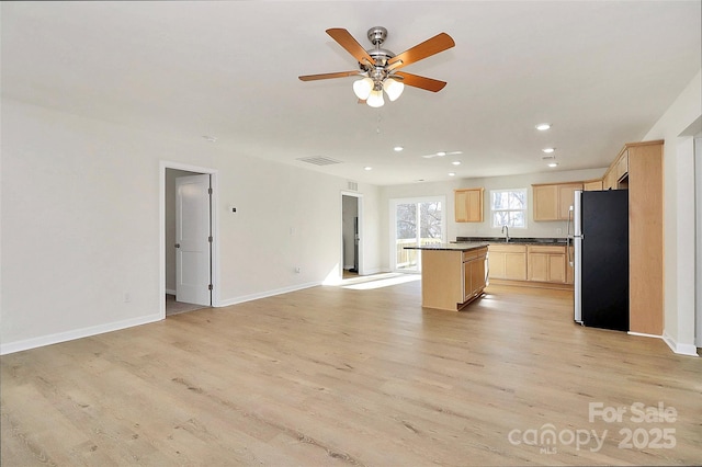 kitchen with light wood-type flooring, stainless steel fridge, light brown cabinets, and a kitchen island