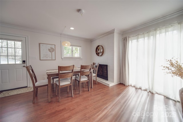 dining room with a brick fireplace, hardwood / wood-style floors, and crown molding