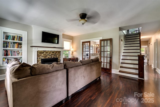 living room with ceiling fan, dark hardwood / wood-style flooring, french doors, a stone fireplace, and built in shelves