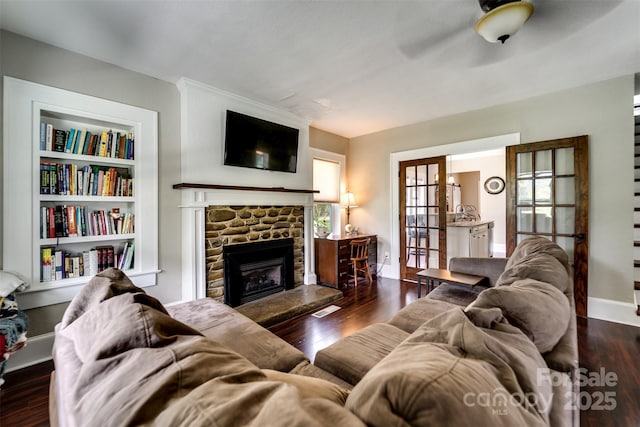 living room with built in features, ceiling fan, dark wood-type flooring, and a fireplace