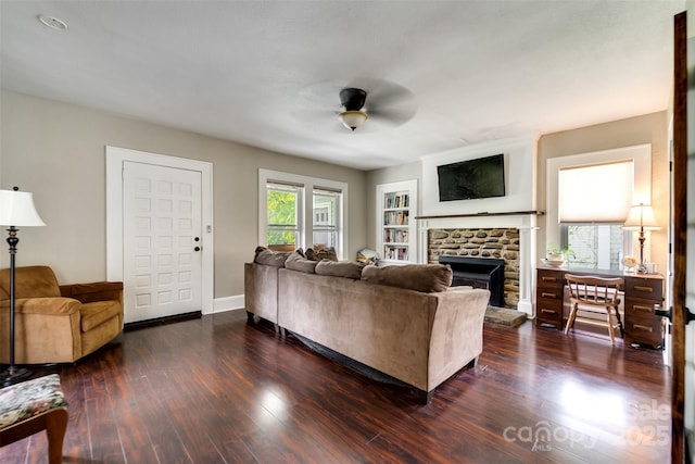 living room featuring dark wood-type flooring, plenty of natural light, ceiling fan, and a stone fireplace