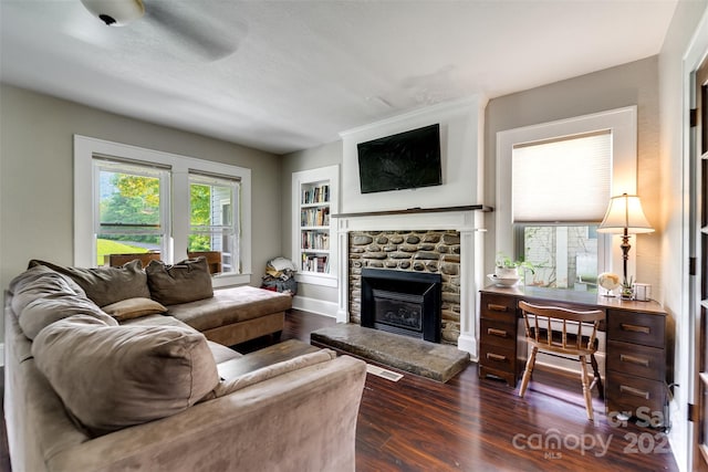 living room featuring built in shelves, dark hardwood / wood-style floors, a wealth of natural light, and a stone fireplace