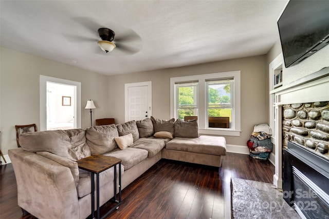 living room featuring ceiling fan, dark hardwood / wood-style floors, and a stone fireplace