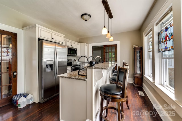 kitchen with a kitchen bar, appliances with stainless steel finishes, white cabinetry, hanging light fixtures, and dark stone counters