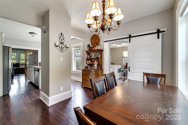 dining room featuring dark wood-type flooring, washer and clothes dryer, a barn door, and an inviting chandelier