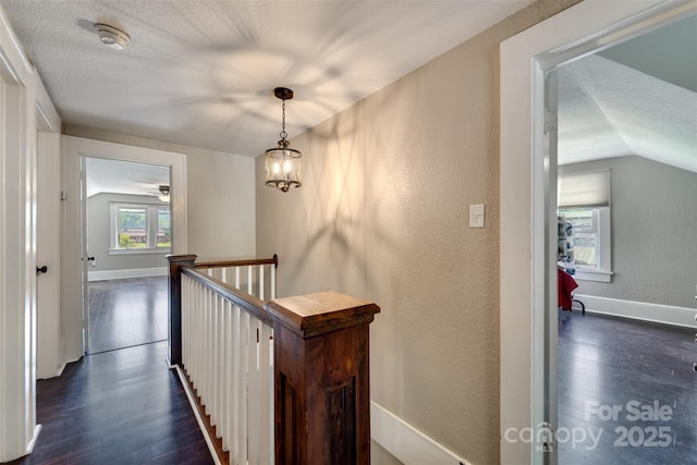 hall featuring dark wood-type flooring, a textured ceiling, and lofted ceiling