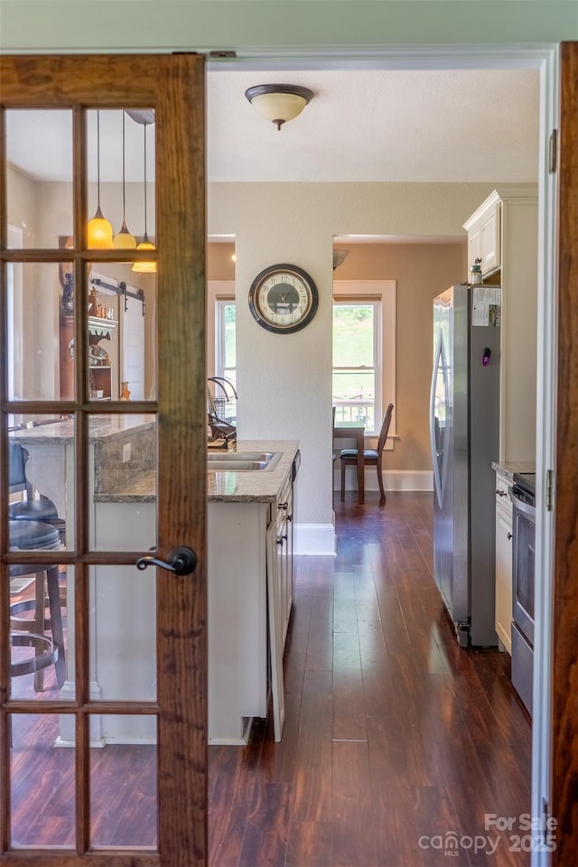 kitchen with appliances with stainless steel finishes, white cabinetry, sink, decorative light fixtures, and dark wood-type flooring