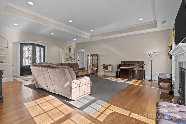 living room featuring a tray ceiling, wood-type flooring, built in shelves, and french doors