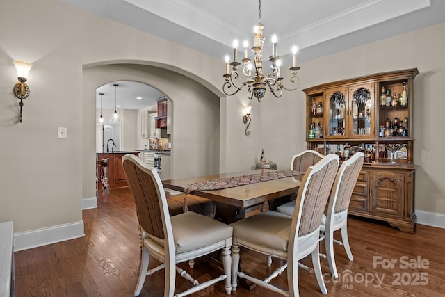 dining area with a raised ceiling, sink, crown molding, and dark hardwood / wood-style floors