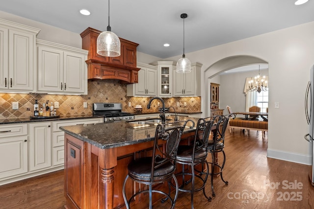 kitchen with sink, stainless steel range, a kitchen island with sink, and decorative light fixtures