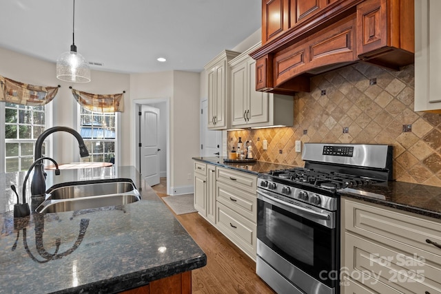 kitchen featuring sink, custom range hood, dark stone counters, stainless steel gas stove, and pendant lighting