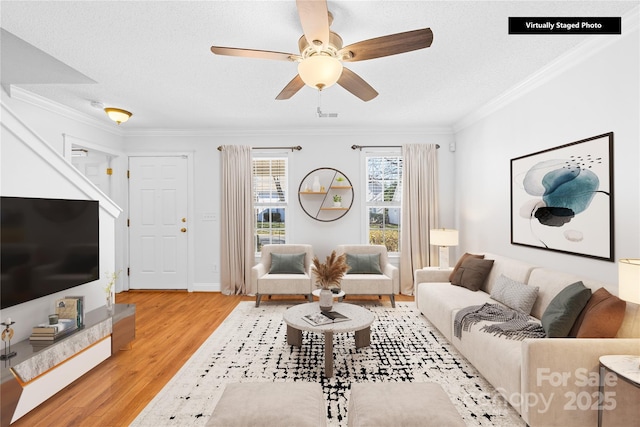 living room with ceiling fan, a textured ceiling, crown molding, and light wood-type flooring