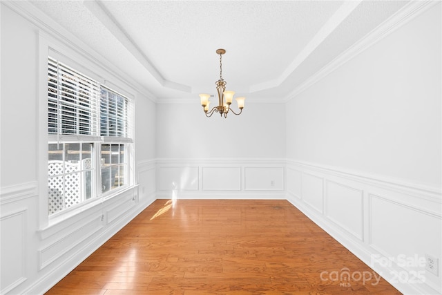 unfurnished dining area featuring hardwood / wood-style flooring, a tray ceiling, a textured ceiling, a chandelier, and crown molding