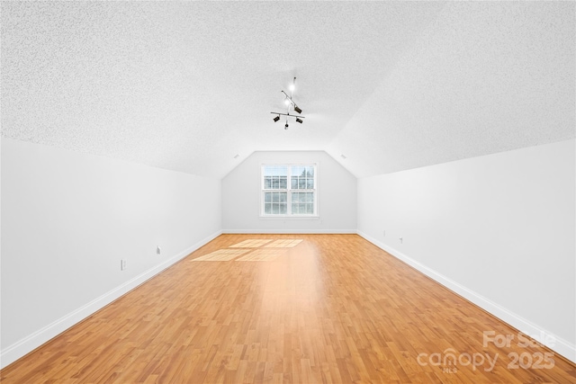 bonus room with vaulted ceiling, a textured ceiling, and light hardwood / wood-style floors