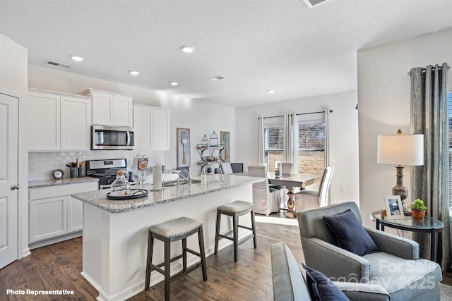 kitchen with appliances with stainless steel finishes, white cabinetry, backsplash, dark hardwood / wood-style floors, and a kitchen island with sink