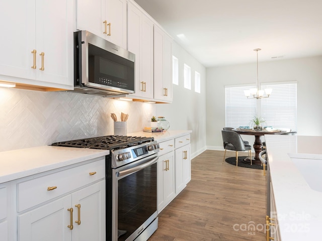 kitchen with white cabinets, decorative light fixtures, stainless steel appliances, a notable chandelier, and light hardwood / wood-style flooring