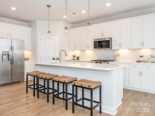 kitchen with white cabinetry, stainless steel appliances, and a center island with sink