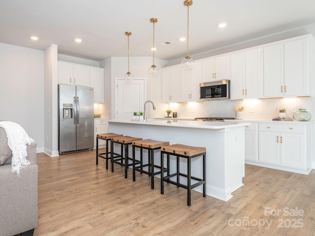 kitchen with decorative light fixtures, white cabinetry, stainless steel fridge, and an island with sink