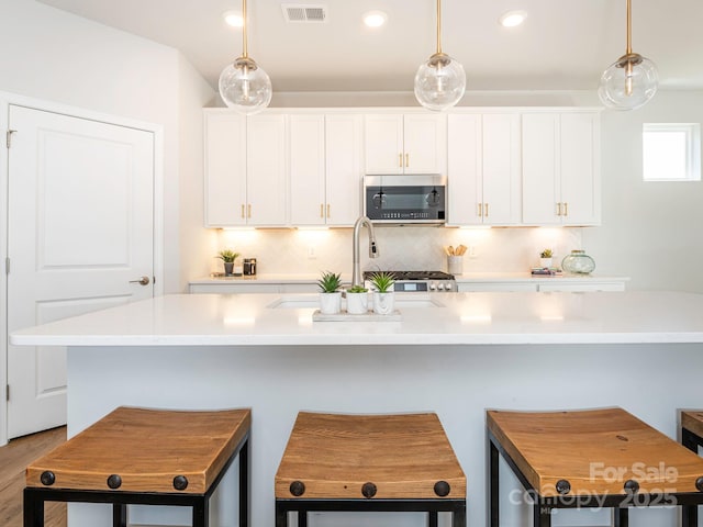 kitchen featuring pendant lighting, white cabinets, and a center island with sink