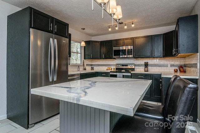 kitchen with a center island, hanging light fixtures, appliances with stainless steel finishes, light tile patterned floors, and light stone counters