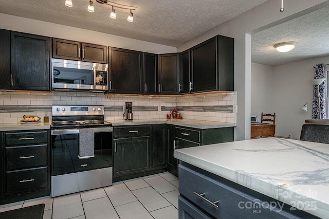 kitchen featuring a textured ceiling, light tile patterned floors, appliances with stainless steel finishes, and decorative backsplash