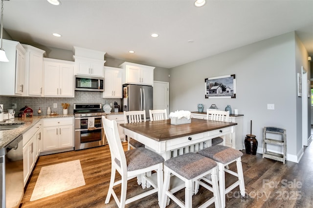 kitchen with dark hardwood / wood-style floors, decorative backsplash, light stone countertops, appliances with stainless steel finishes, and white cabinets