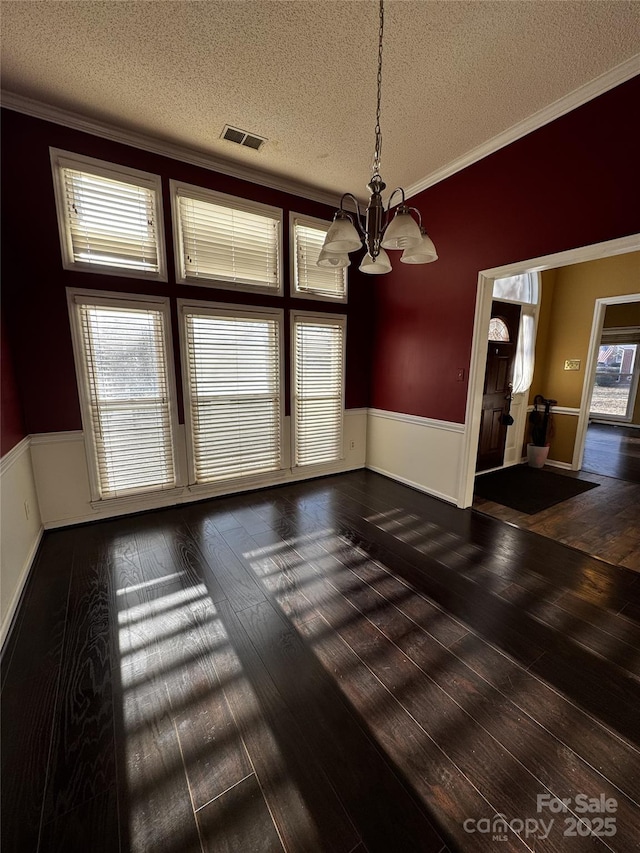 unfurnished dining area featuring an inviting chandelier, crown molding, dark hardwood / wood-style floors, and a textured ceiling