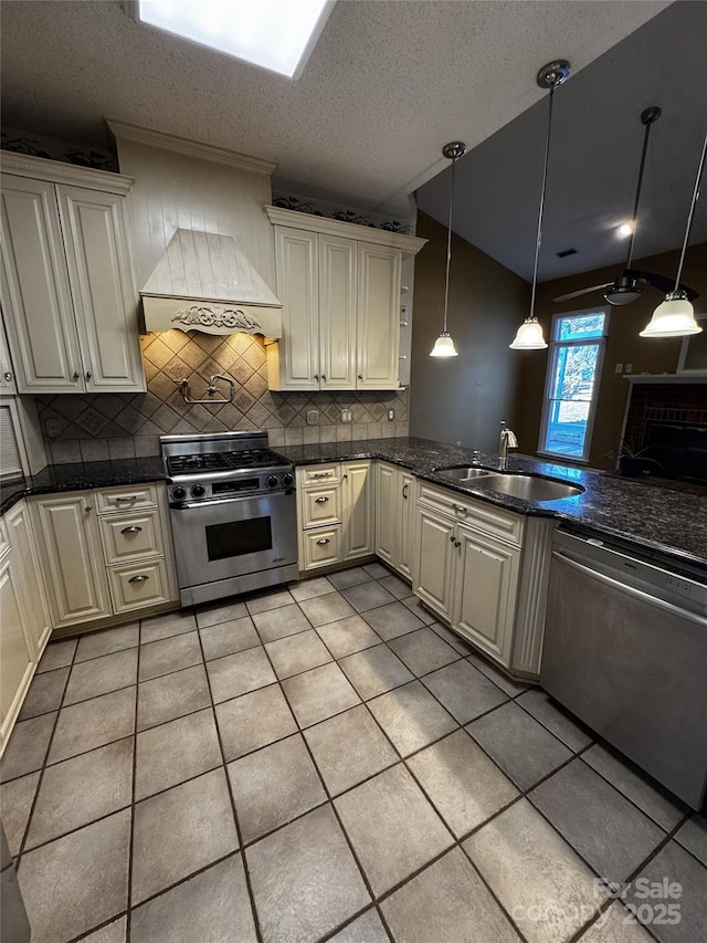 kitchen featuring sink, hanging light fixtures, custom range hood, stainless steel appliances, and cream cabinetry