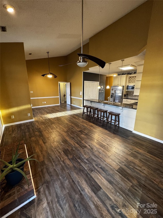 kitchen with pendant lighting, dark wood-type flooring, a breakfast bar area, stainless steel appliances, and a textured ceiling