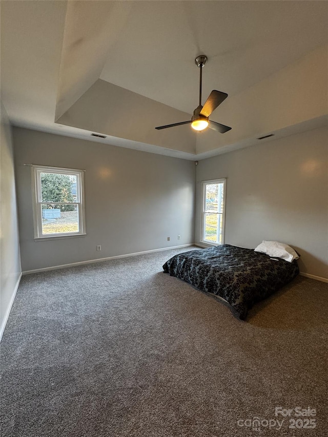 carpeted bedroom with multiple windows, a tray ceiling, and ceiling fan