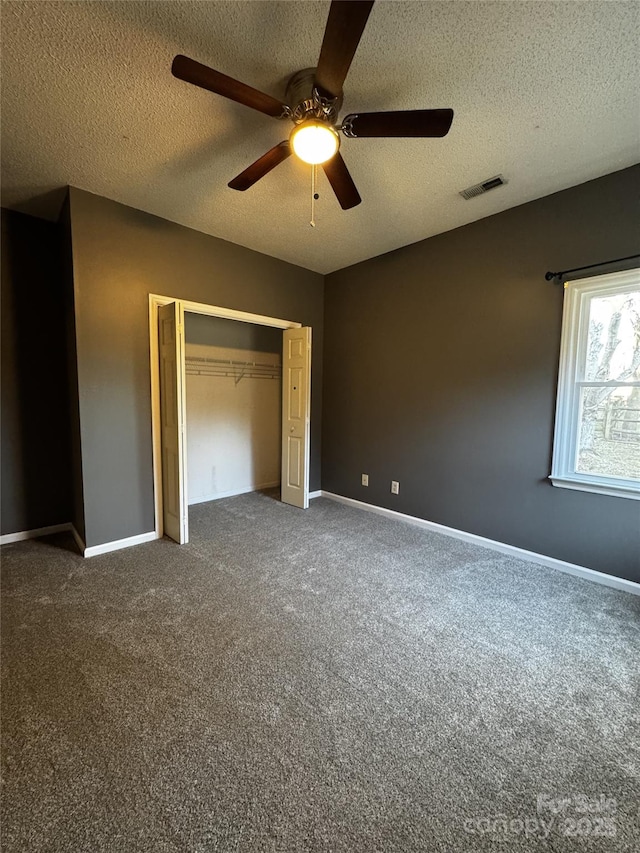 unfurnished bedroom featuring a textured ceiling, a closet, ceiling fan, and dark colored carpet