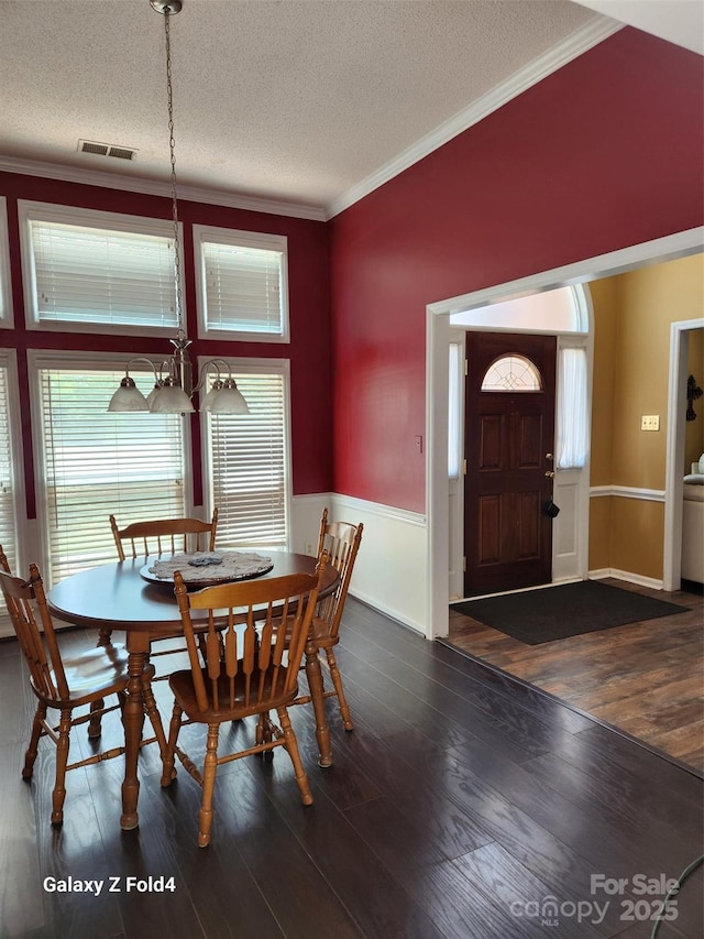 dining space with dark wood-type flooring, ornamental molding, and a textured ceiling