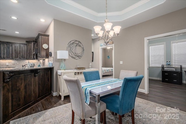 dining room with crown molding, dark hardwood / wood-style flooring, a raised ceiling, and a chandelier