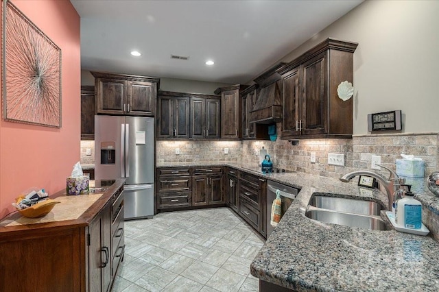 kitchen with custom range hood, sink, appliances with stainless steel finishes, light stone counters, and dark brown cabinetry